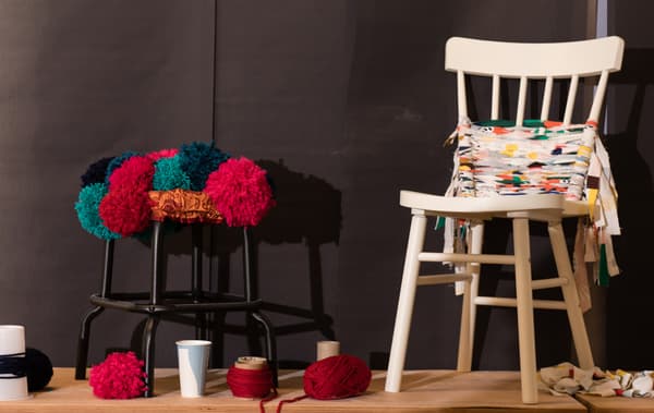 Un tabouret noir recouvert de pompons en laine et une chaise blanche recouverte de bandes de tissu.