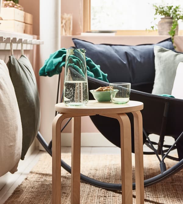 Un taburete de madera FROSTA utilizado como mesa auxiliar en un agradable salón.