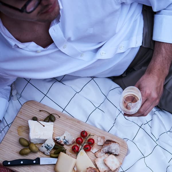 Un tagliere in legno con dei finger food, come formaggi, olive e cracker, su un copripiumino e un uomo sdraiato accanto - IKEA