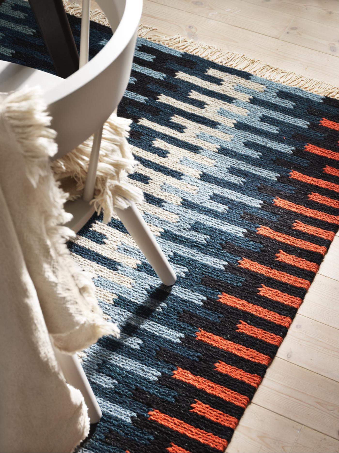 Un tapis multicolore en laine, vu d’en haut, dans différentes nuances de bleu et de rouge, et une chaise blanche
