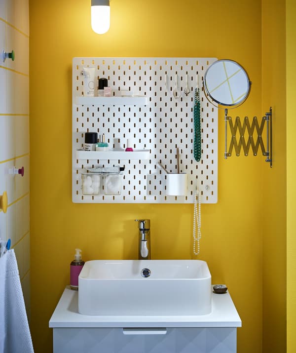 Un tauler perforat SKÅDIS sobre un lavabo blanc i un mirall extensible FRÄCK a un bany petit.