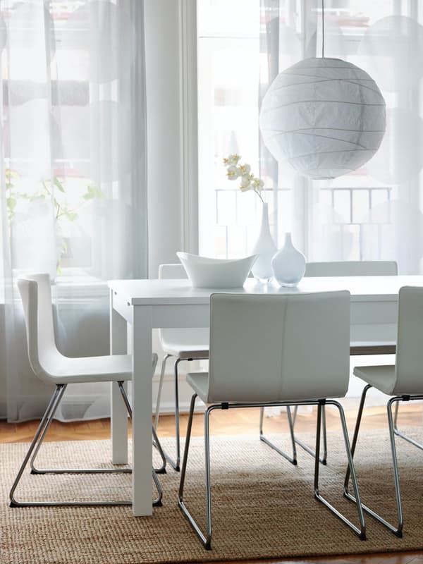 Un tavolo bianco con tre sedie su un tappeto beige in mezzo a una stanza con le tende bianche. 