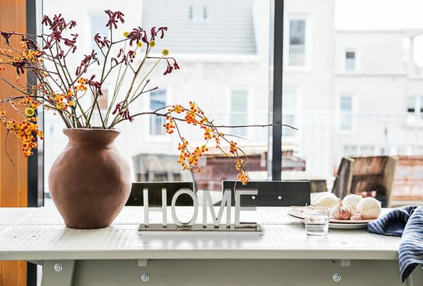 Un tavolo con fiori in vaso, un bicchierino d'acqua con affianco due piatti con dell'aglio sopra e un asciugamano nero. In mezzo, un oggetto con la scritta 