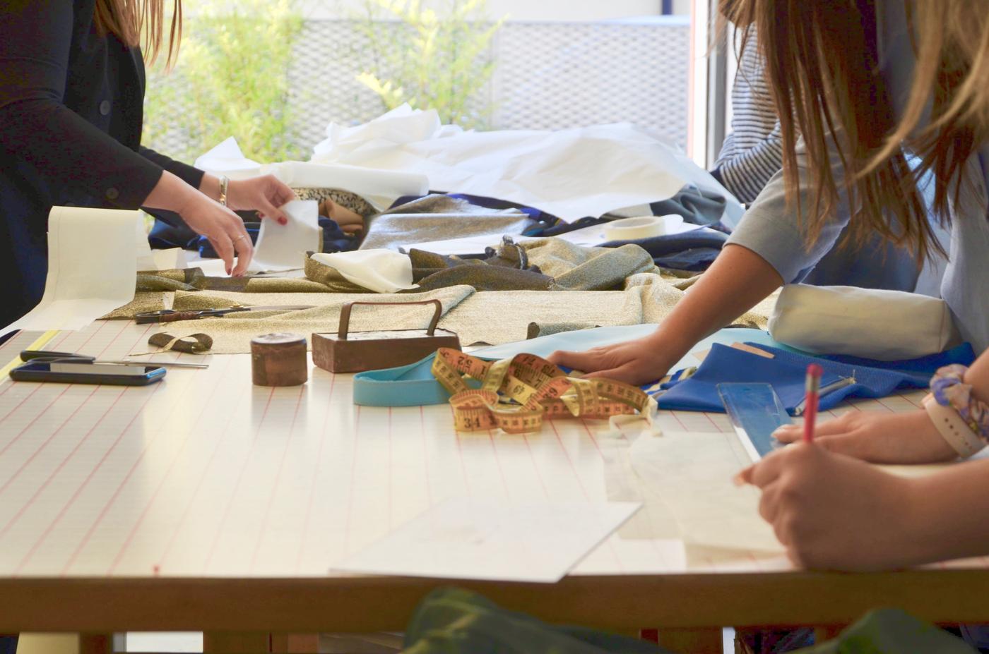 Un tavolo con tre persone che scrivono e lavorano su materiali tessili.