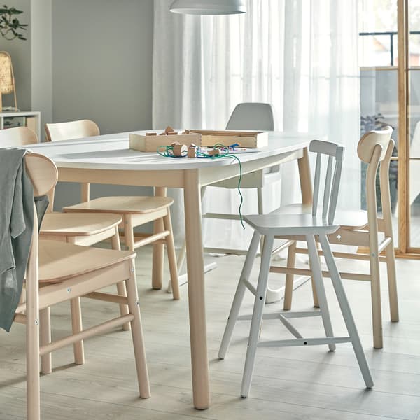 Un tavolo da pranzo con sopra alcuni lavoretti fatti dai bambini, sedie in betulla, un seggiolone e una sedia junior con poggiapiedi - IKEA
