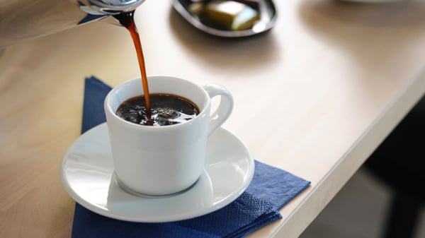 Un tazzina che su un tavolo che viene riempito di caffé. 