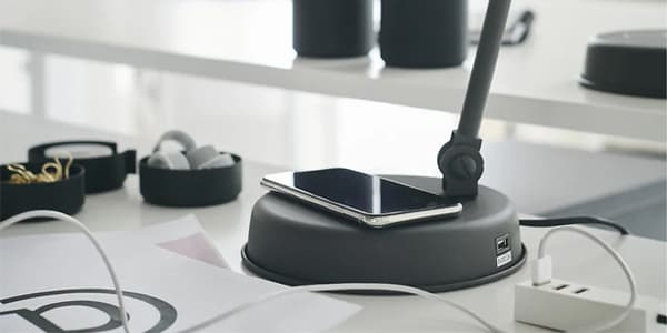 Un telèfon sobre la base d’un llum d’escriptori gris fosc en un escriptori blanc.