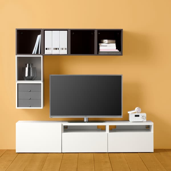 Un téléviseur entouré par trois côtés d’un agencement de rangements BESTÅ et EKET géométrique, mais asymétrique, contre un mur jaune.