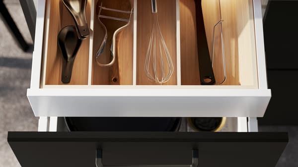 Un tiroir de cuisine à façade blanche est ouvert, révélant des ustensiles de cuisine dans un range-couverts UPPDATERA en bambou clair.