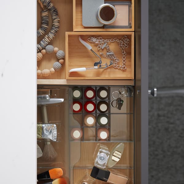 Un tiroir de salle de bain ouvert contenant un organiseur en plastique transparent avec du maquillage, et des boîtes en bambou DRAGAN avec des accessoires.