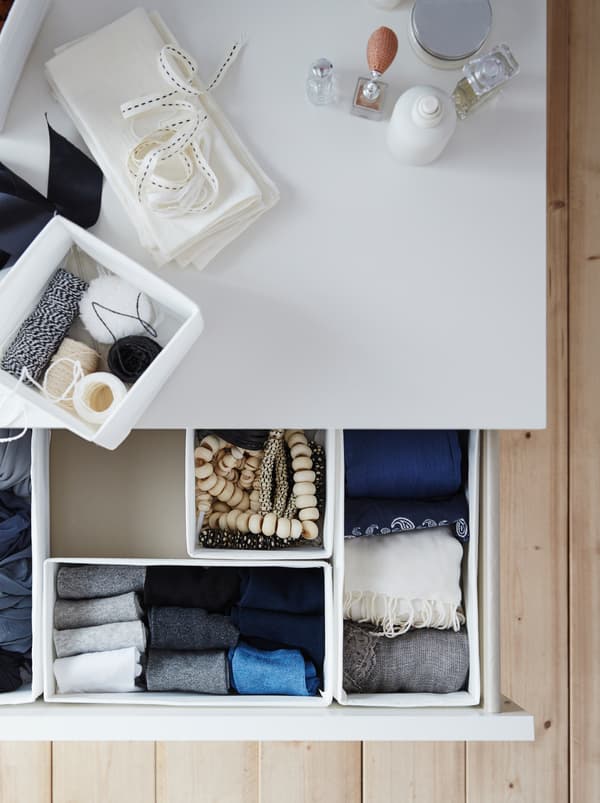 Un tiroir ouvert dans une chambre avec des inserts de boîtes SKUBB blancs remplis de colliers, de chaussettes pliées avec soin et de foulards.