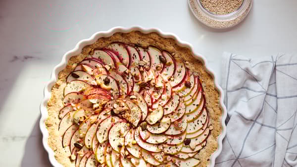 Un torchon de cuisine blanc orné d’un motif gris graphique et une tarte couverte de fines tranches de pommes dans un moule à tarte VARDAGEN blanc.