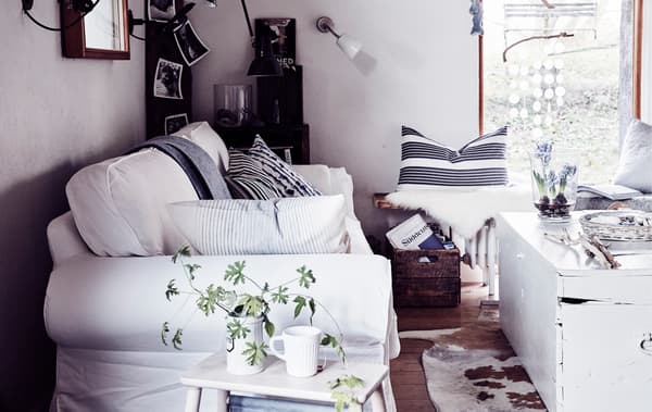 Un tradizionale divano bianco in soggiorno con cuscini a righe, un baule vintage in legno e materiali naturali – IKEA
