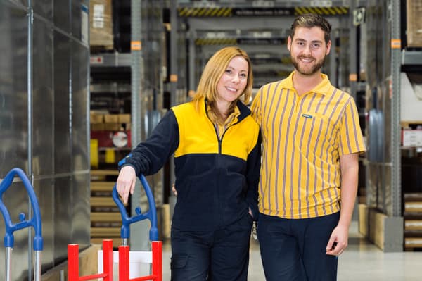 Un treballador i una treballadora d’IKEA abraçant-se i fent-se una foto mentre agafen un carro, en un magatzem amb caixes.