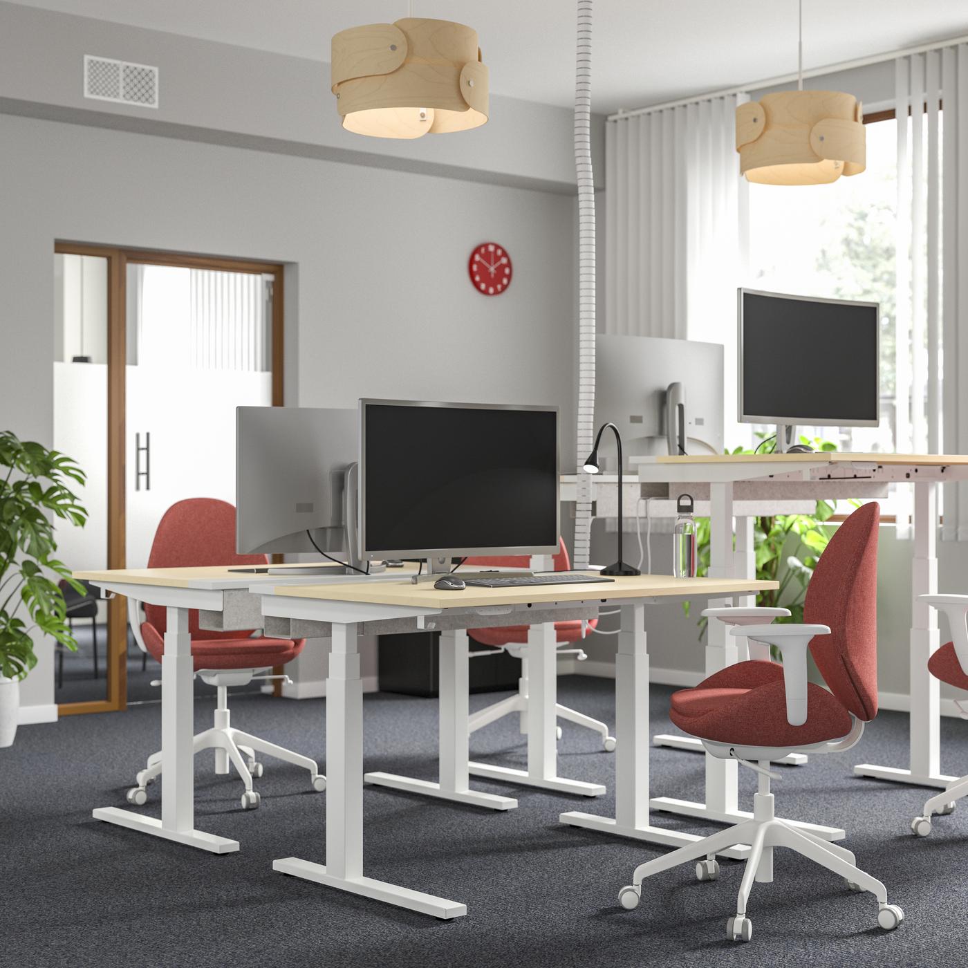 Un ufficio con diverse scrivanie e sedie rosse con gambe bianche girevoli