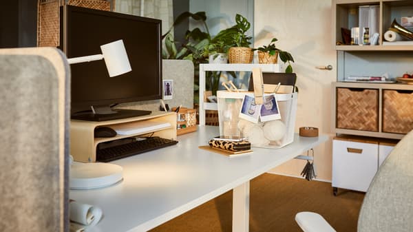 Un ufficio delicatamente illuminato con una scrivania regolabile in altezza TROTTEN dotata di un supporto per PC portatile VATTENKAR e uno scaffale per scrivania VATTENKAR - IKEA