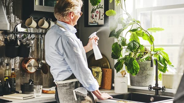 Un uomo che sta innaffiando con uno spruzzino alcune piante sul davanzale in cucina.