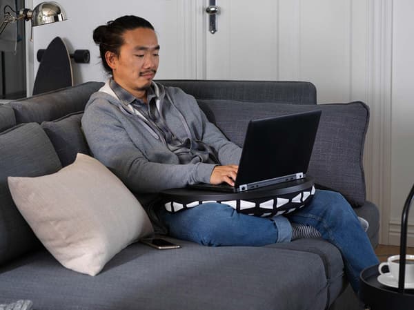 Un uomo è seduto con il suo computer portatile aperto sulle ginocchia su un divano grigio scuro con un tavolino davanti su cui c'è una tazza di caffè.