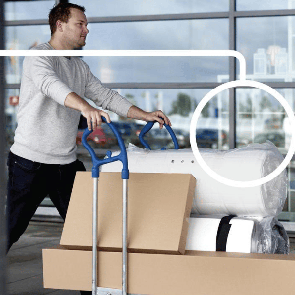 Un uomo spinge in avanti un carrello della spesa ikea con prodotti in confezione piatta.