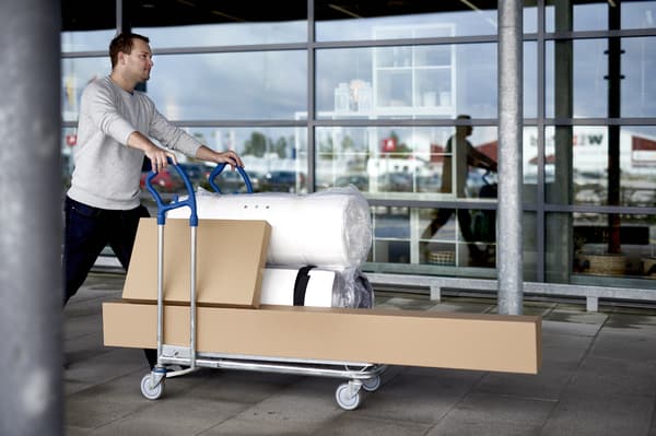 Un uomo sta spingendo un carrello con molti pacchi piatti IKEA e un materasso arrotolato davanti a un negozio IKEA.