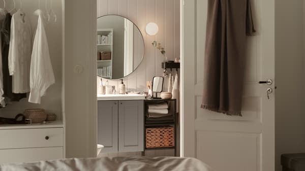 Un vanitorio ENHET/TVÄLLEN con dos puertas con un espejo redondo encima, en un baño pequeño junto a un dormitorio.