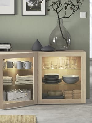 Un vase transparent posé sur un meuble de rangement BESTA avec des portes vitrées SINDVIK en chêne.