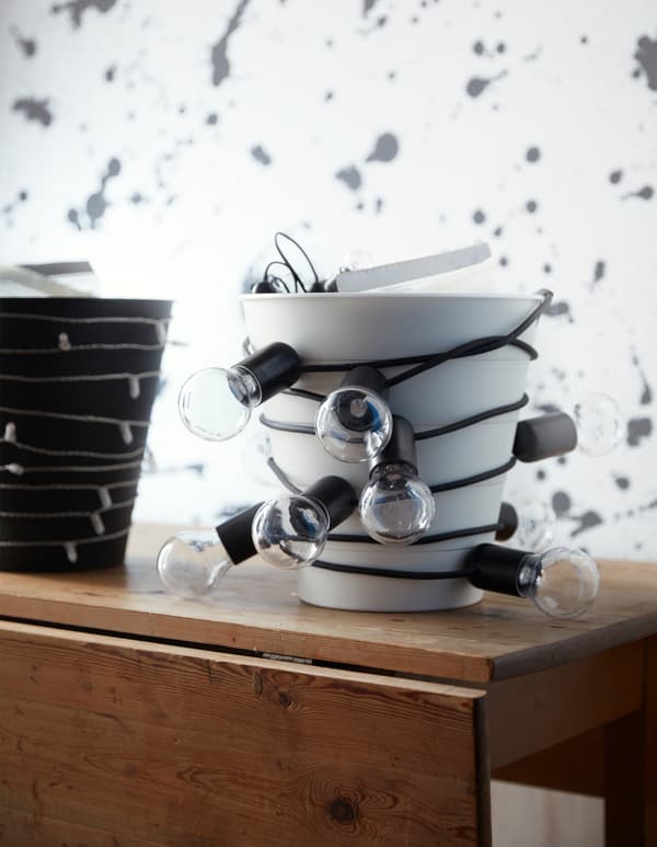 Un vaso FNISS in colore bianco avvolto da cavi e lampadine sopra un mobile in legno.  