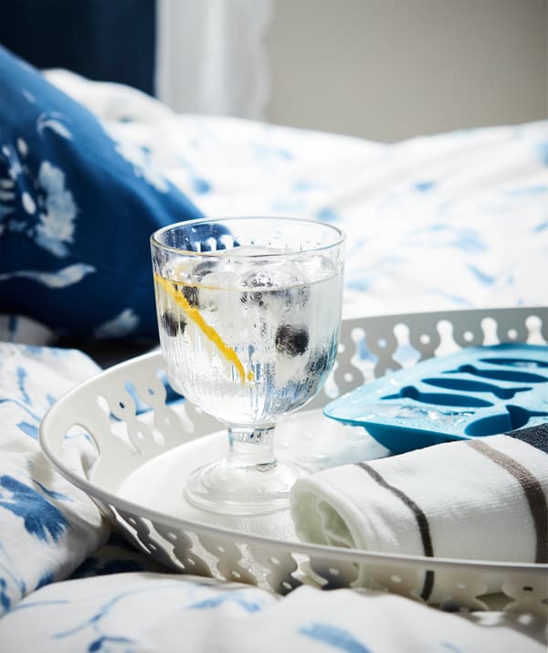 Un vassoio con un bicchiere d'acqua con ghiaccio e mirtilli, un asciugamano arrotolato e una vaschetta per il ghiaccio su un letto morbido e invitante.
