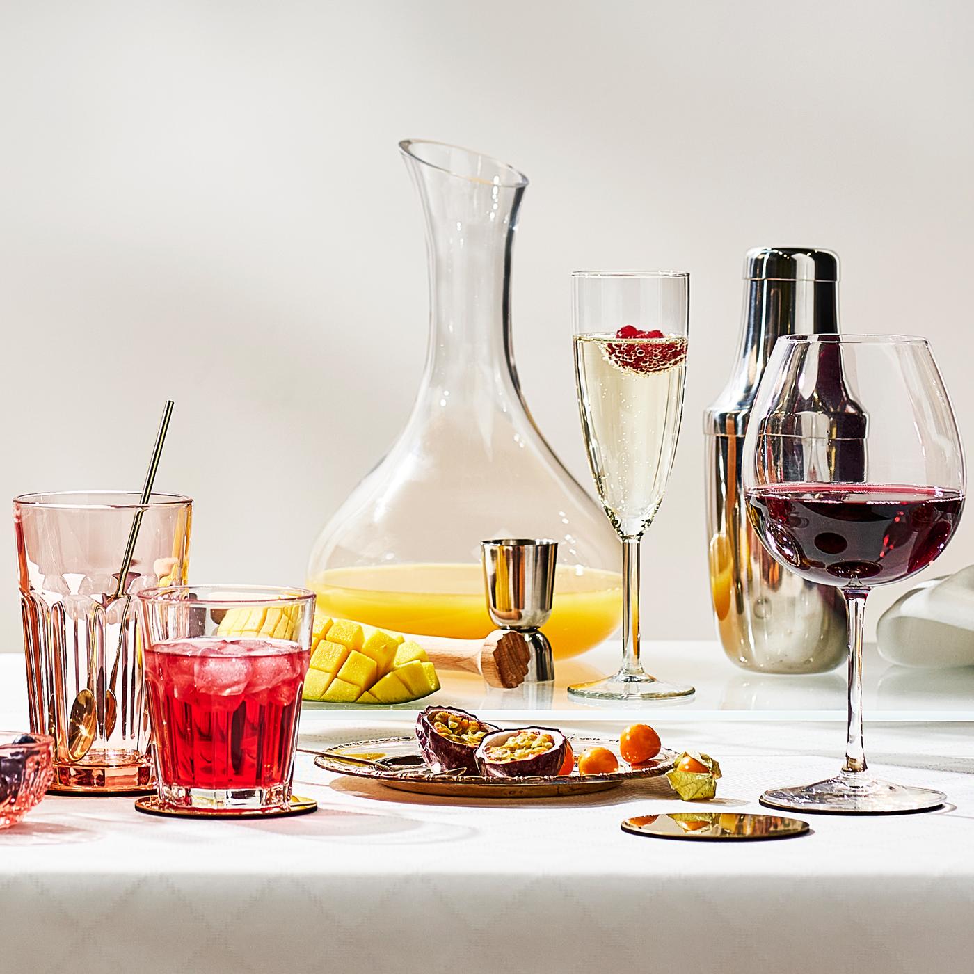 Un verre à vin, une flûte à champagne, deux verres à eau et une carafe en verre transparent sur une table revêtue d’une nappe blanche.