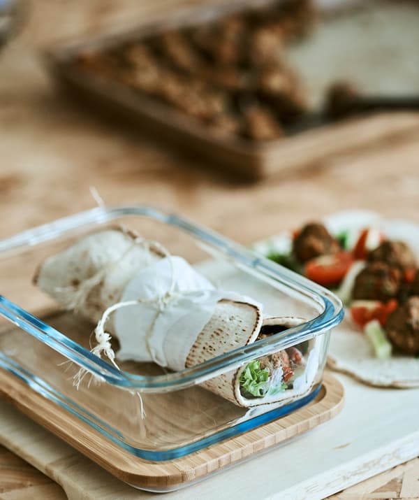 Un wrap cu tortilla înfășurat într-un recipient de sticlă, lângă o tortila desfăcută, cu ingrediente sățioase. 