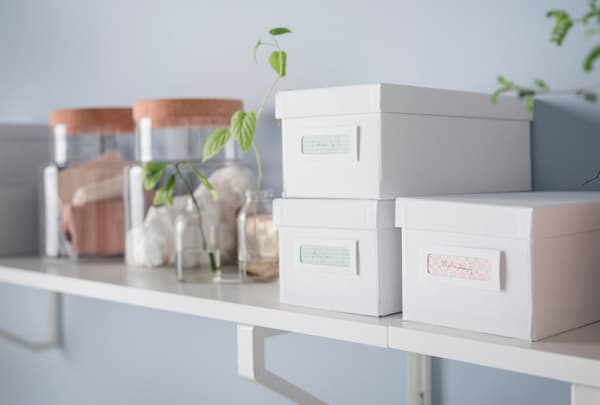 Una balda de madera blanca y clara con ajas y tarros para guardar cosas.