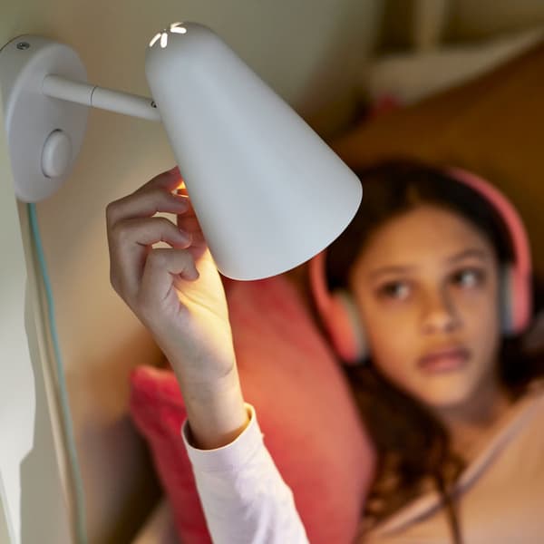 Una bambina che indossa cuffie per la musica, mente regola la luce di un faretto.