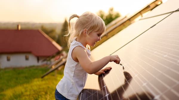 Una bambina con i capelli biondi fa scorrere l'estremità di una spiga sulla superficie di un pannello solare all'aperto durante il tramonto - IKEA.