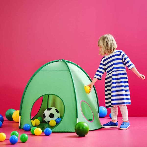 Una bambina gioca con delle palline colorate e un pallone da calcio e una tenda giocattolo verde. 