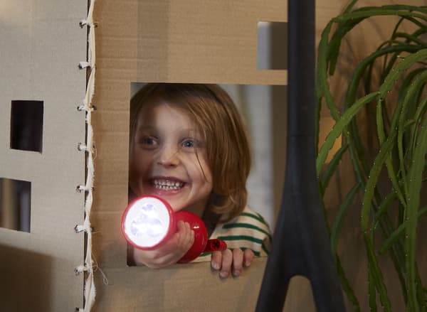 Una bambina sorridente che gioca a nascondino tenendo in mano una torcia manuale LJUSA rossa.