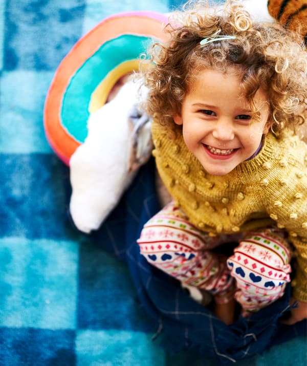 Una bambina sorridente seduta su un tappeto a quadri e un plaid blu scuro - IKEA