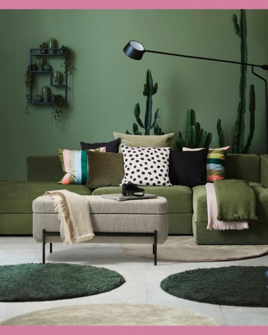 Una banca acolchada IKEA frente a un sofá en una sala convtonos verdes.