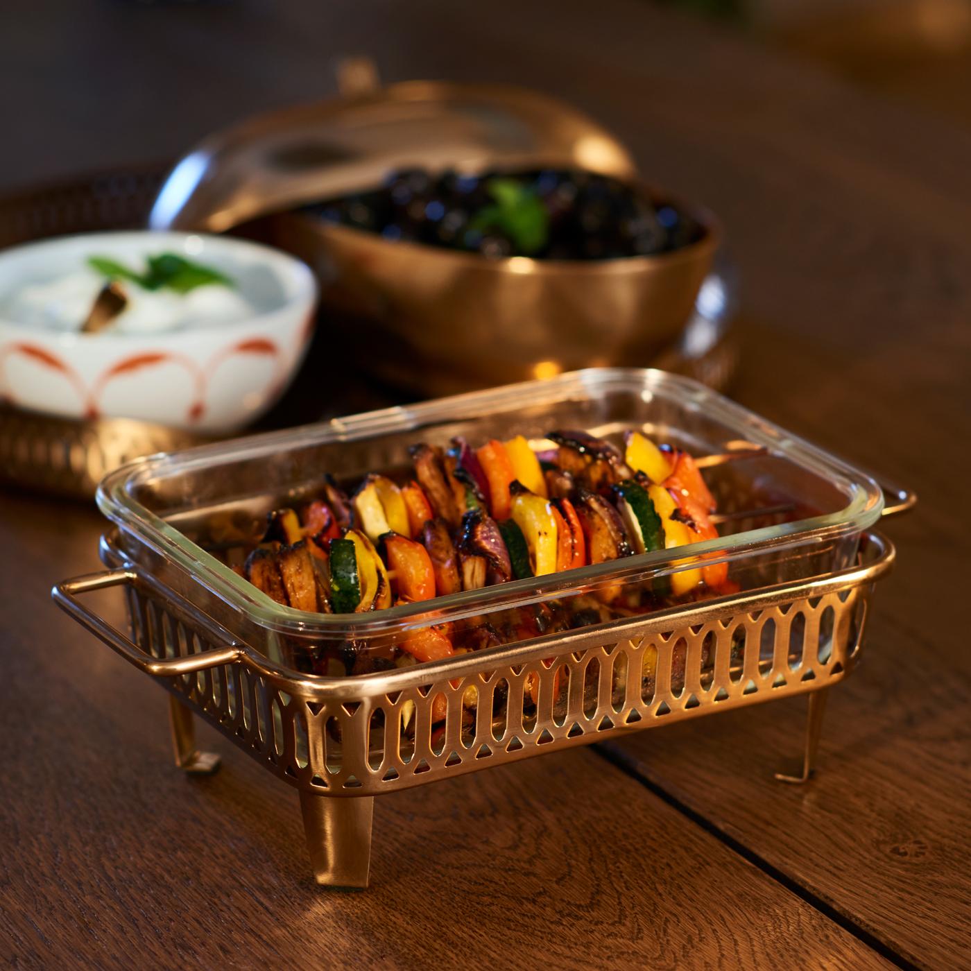 Una bandeja GOKVÄLLÅ en la que se ha colocado un recipiente de cristal y dos pinchos morunos.