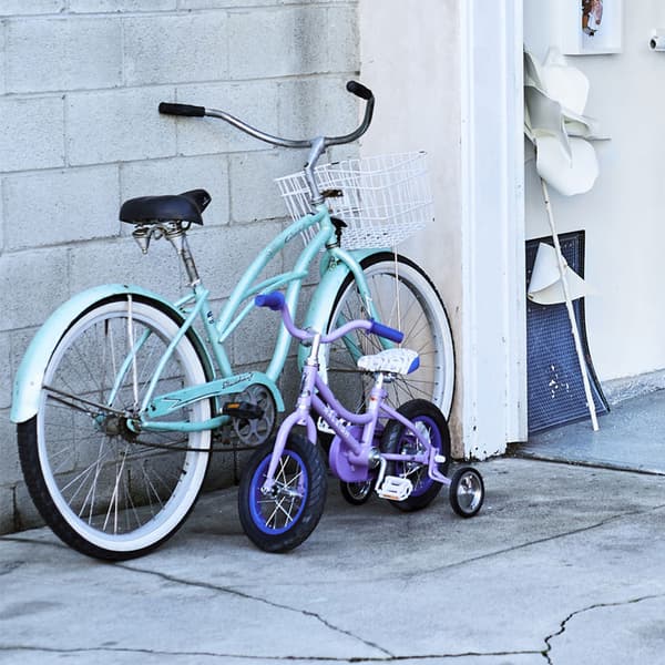 Una bicicletta da adulto turchese e una da bambino lilla vicine ad un muro.