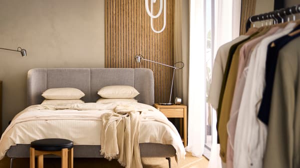 Una cama doble TUFJORD con almacenaje vestida con ropa de cama NATTJASMIN beige y una manta VALLKRASSING encima.