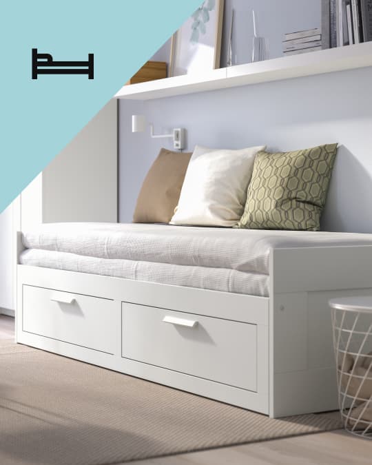 Una cama para invitado en una sala con cojines sobre el colchón y en el costado superior izquierdo de la foto un ícono de cama.