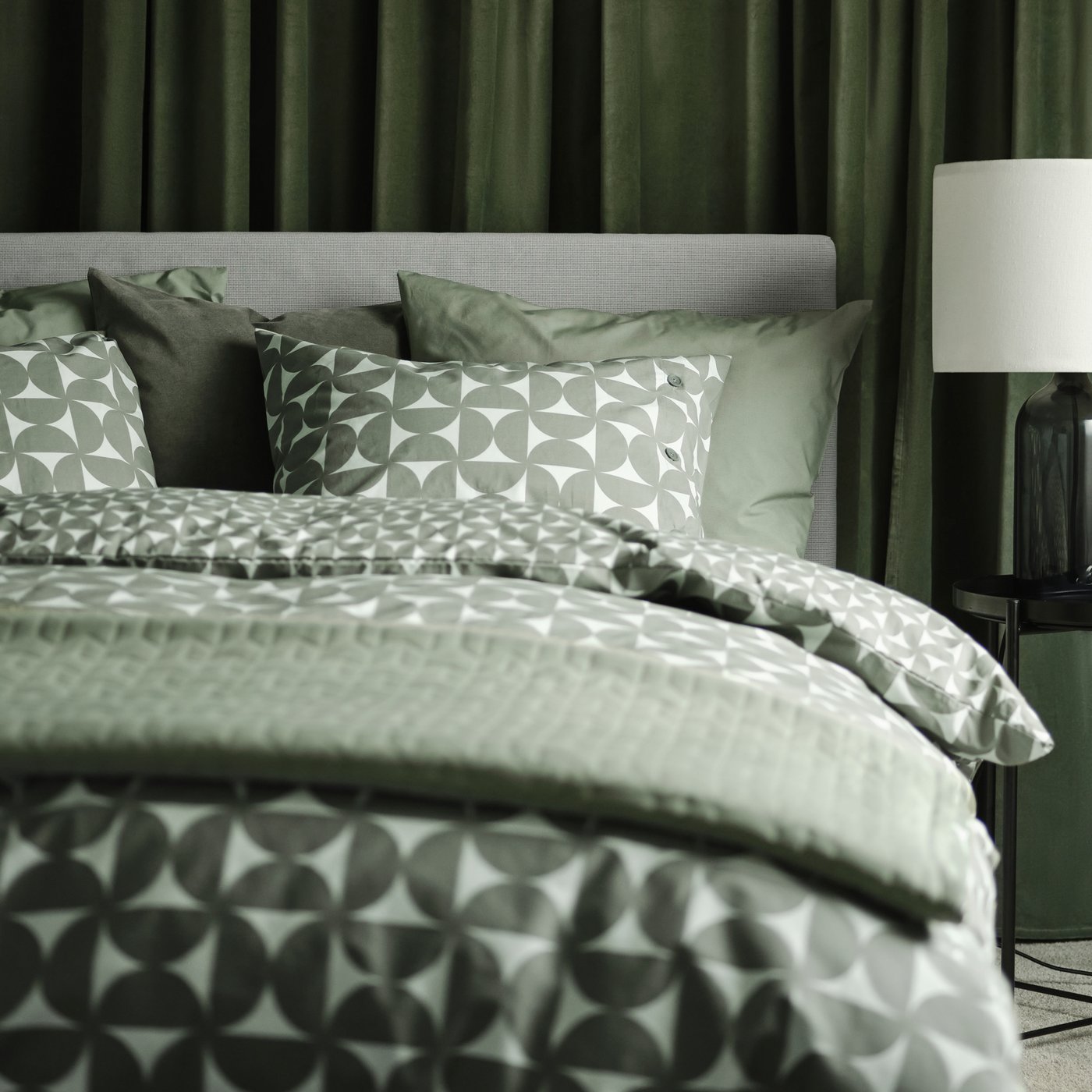 Una cama tapizada GLADSTAD en Kabusa gris claro con cuatro cajas de almacenaje con ropa de cama ÄNGSNEJLIKA en gris/verde.