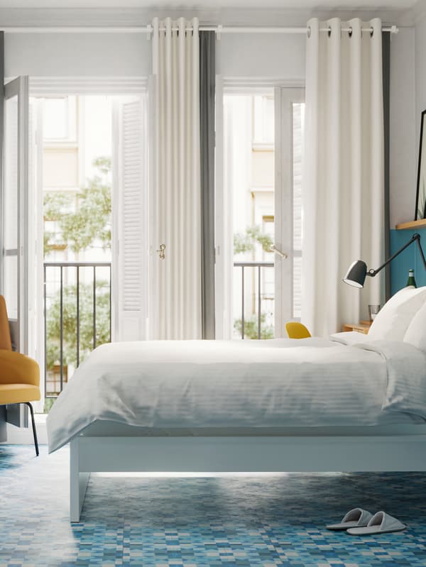 Una camera con un letto bianco e biancheria da letto bianca, pareti e pavimenti dipinti di blu e grandi portefinestre che danno su un balcone.