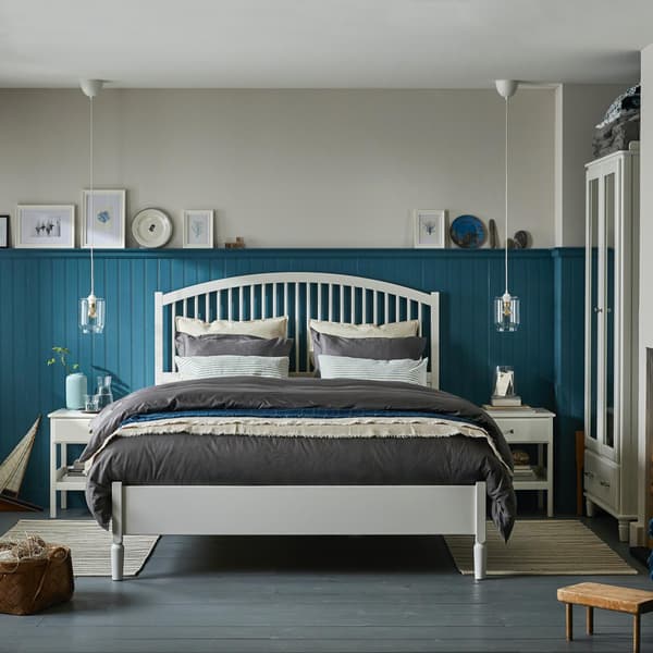 Una camera da letto con due una parete azzurra e bianca. Nella parte bianca sono appesi dei quadri e un orologio. Accanto al letto due comodini TYSSEDAL.