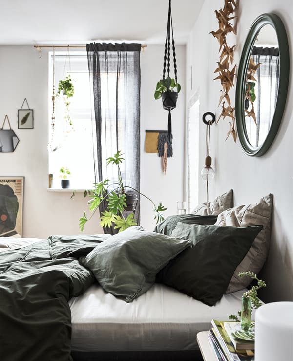 Una camera da letto con le pareti bianche, biancheria da letto verde e piante in vaso - IKEA