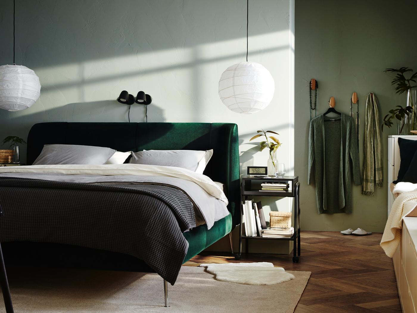 Una camera da letto con letto imbottito TUFJORD verde contro una parete e due lampade a sospensione appese al soffitto .