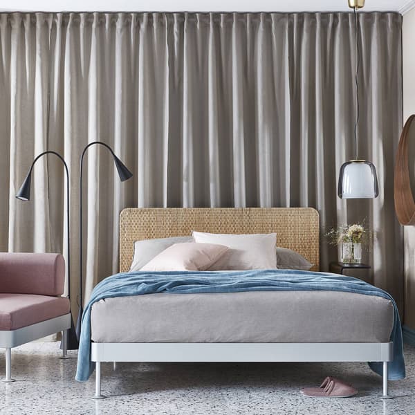 Una camera da letto con una tenda. Al centro della stanza con una struttura letto DELAKTIG con accanto una poltrona e un comodino.