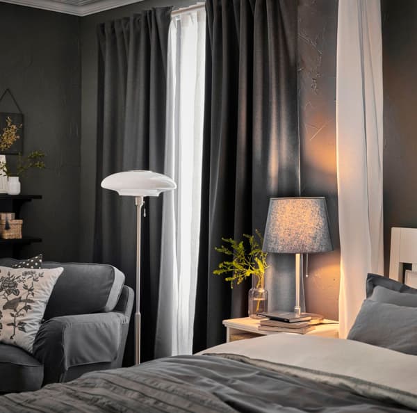 Una camera da letto sui toni del grigio e del bianco. Ci sono due lampade, un divano e un bianco comodino accanto al letto.