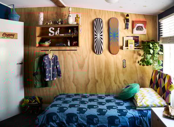 Una cameretta con mensole e skateboard su una parete di legno e un letto con biancheria a motivo grafico blu.