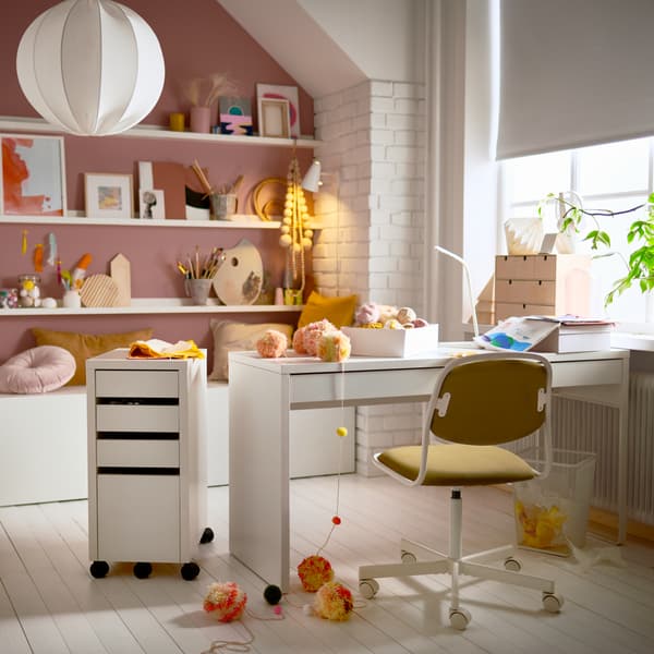 Una cameretta con una scrivania MICKE bianca, una sedia da scrivania per bambini, una cassettiera bianca e mensole per quadri con decorazioni.